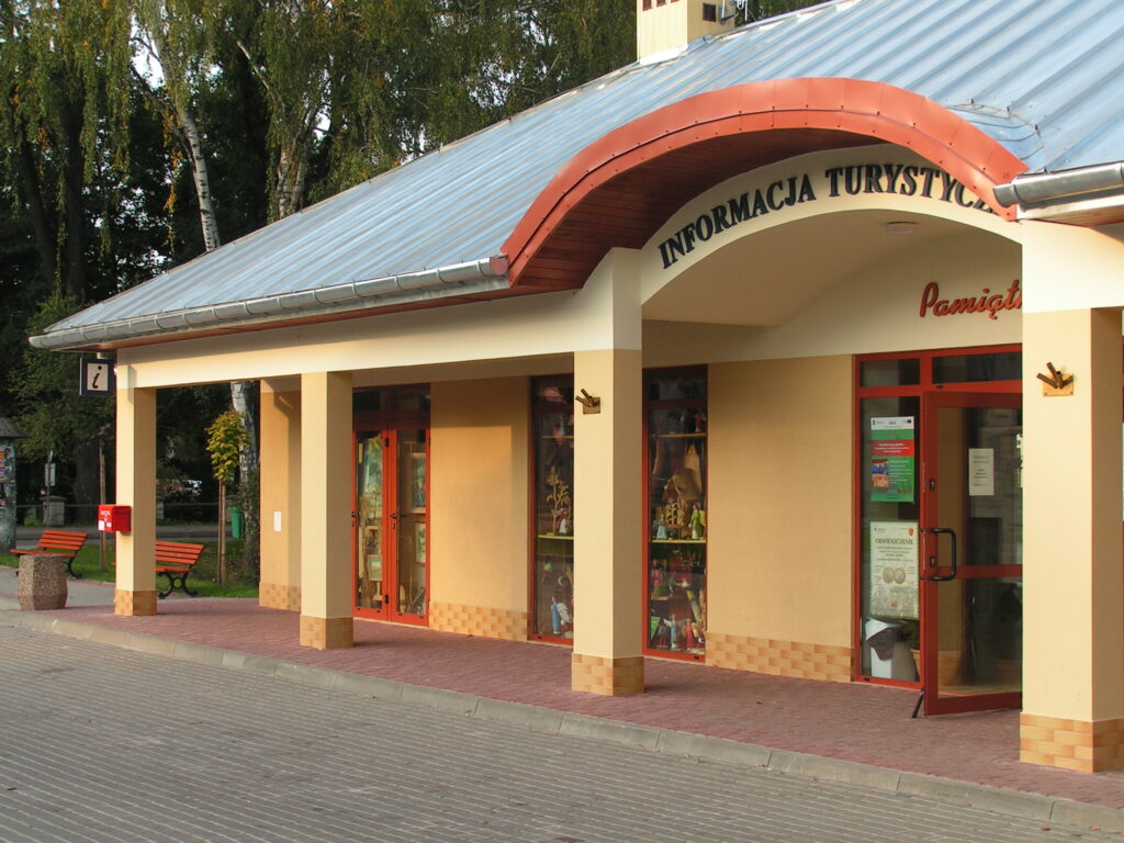 informacja turystyczna w Krasnobrodzie. Żółty budynek z filarami i szklanymi witrynami.